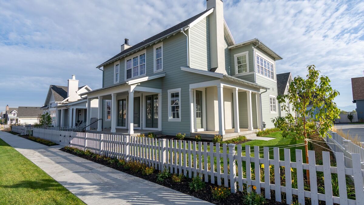 A white vinyl picket fence running along a sidewalk in front of a new two-story home